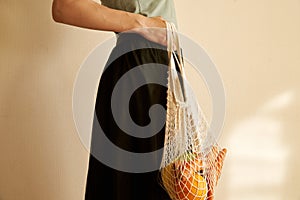 Woman hand holding a string shopping bag with vegetables, fruits in warm earthy tones, zero waste