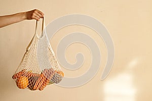 Woman hand holding a string shopping bag with vegetables, fruits in warm earthy tones, zero waste