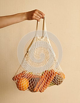 Woman hand holding a string shopping bag with vegetables, fruits in warm earthy tones, zero waste