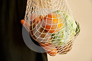 Woman hand holding a string shopping bag with vegetables, fruits in warm earthy tones, zero waste