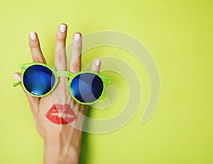 Woman hand holding sunglasses on bright green background, cosmetic or vacation concept