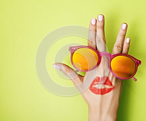 Woman hand holding sunglasses on bright green background, cosmetic or vacation concept