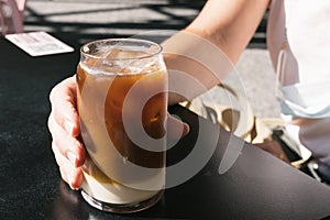 Woman hand holding tasty glass of cold brew coffee with milk