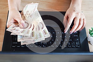 Woman hand holding Thai banknotes and working on computer laptop from home, make money online,earning,investment concept