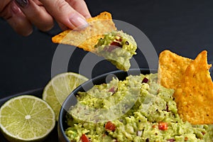 Woman hand holding tortilla chip or nachos with tasty guacamole dip on a black background
