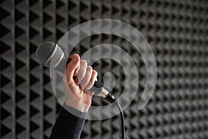 Woman hand holding vocal mic on acoustic foam panel background