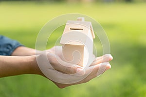 Woman hand is holding the wood house model on a blurred background in the public park