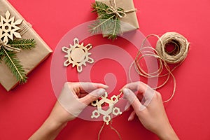 Woman hand holding wooden handmade snowflake over Christmas background with presents wrapped kraft paper and fir branches, twine,