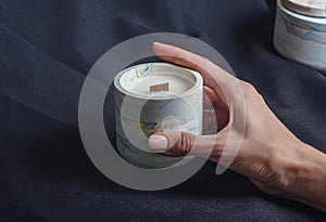 Woman hand holds a decorative scented candle on a black background