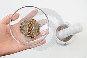 Woman hand holds a glass sauser with ground pepper over marble or granite mortar with pestle on a white kitchen table. Modern