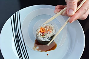 Woman hand holds one Makizushi sushi fresh maki roll with chopsticks