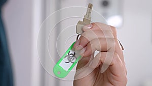 Woman hand holds shiny key to door with biohazard emblem drawn on green plastic breloque in light room extreme close