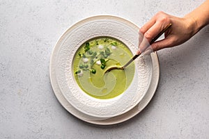 Woman hand holds spoon on soup puree of green peas