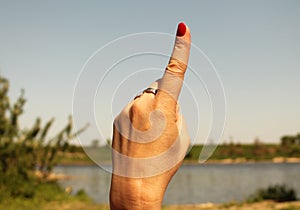 Woman hand with the index finger pointing up against the backdrop of summer water