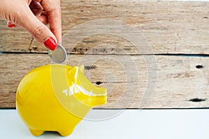 Woman hand inserting coin in a yellow piggy bank, savings for future concept