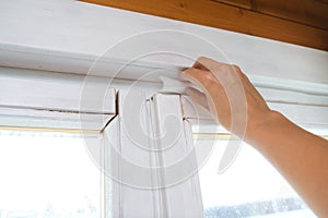 Woman hand insulating old windows to prevent warmth heat leak and drafts, preparing house for winter and cold weather