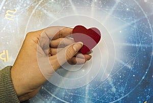 Woman hand keeping a red heart over blue horoscope like astrology, zodiac and love concept