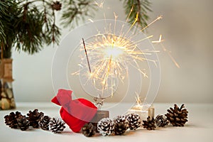 woman hand lighting festive sparkles near pine cones, christmas tree and red christmas hat. New year party burning