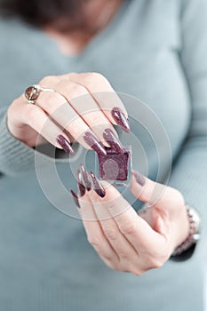 Woman hand with long nails and a bottle of brown bordo nail polish