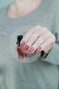 Woman hand with long nails and a bottle of brown red nail polish