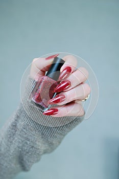 Woman hand with long nails and a bottle of brown red nail polish