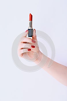 Woman hand with long red manicure on nails holding red lipstick on white background