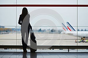 Woman with hand luggage in international airport, looking through the window at planes