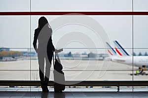 Woman with hand luggage in international airport, looking through the window at planes