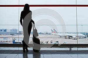 Woman with hand luggage in international airport, looking through the window at planes