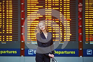 Woman with hand luggage in international airport terminal, looking at information board