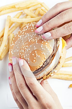 Woman hand with manicure holding big burger french fries on background, people eating food concept