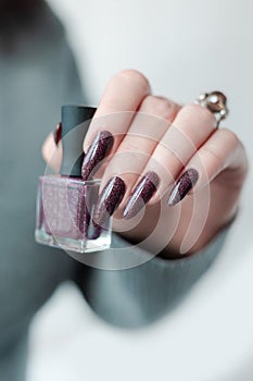 Woman hand with nails and a bottle of dark brown red nail polish