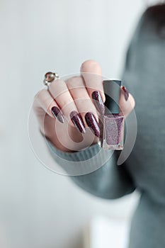 Woman hand with nails and a bottle of dark brown red nail polish