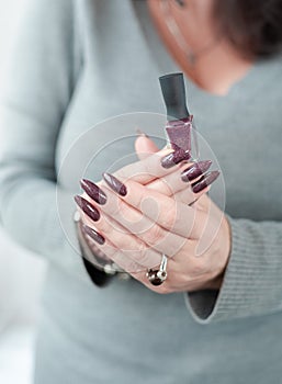 Woman hand with nails and a bottle of dark brown red nail polish