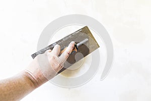Woman hand with old metal spatula to equalize plaster filler on the wall