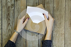 Woman hand opening envelope on wooden table.