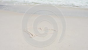 Woman hand paint heart symbol on beach sand and water wash it out