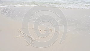 Woman hand paint heart symbol on beach sand and water wash it out