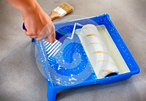 Woman hand with paint roller and paint tray with primer.