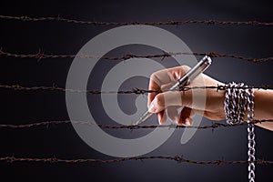 Woman hand with pen tied with chain and rusty sharp bare wire, depicting the idea of freedom of the press or expression. World