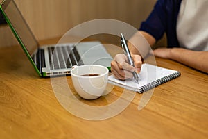 Woman hand with pen writing on notebook at coffee shop