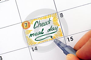 Woman hand with pen writing reminder Cheat Meal Day in calendar