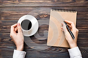 Woman hand with pencil writing on notebook and hold coffee cup. Woman working on office table with coffee