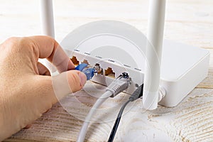 Woman hand plugging a blue network cable into socket of a white Wi-Fi wireless router on a white wooden table. Wlan router with