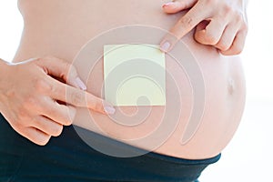 Woman hand posting empty adhesive note on her pregnancy belly