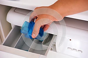 Woman hand pouring liquid detergent in a washing machine