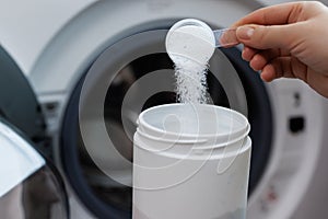 Woman hand pouring washing powder. Measuring cup with granular solid detergent. Open washing machine