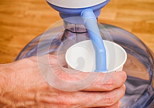 Woman hand pouring water in paper cup from bottle with water pump