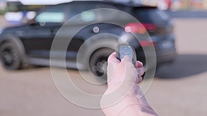 Woman hand presses on the remote control car alarm systems. Female holding car keys with black car on background