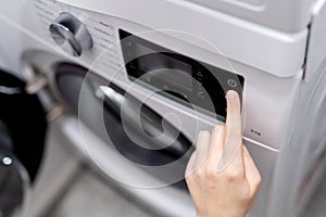 Woman hand pressing start button on automatic washing machine for daily laundry.